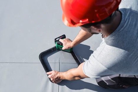 A man wearing a red hard hat is working on a roof.