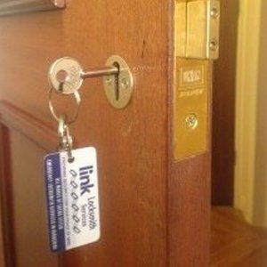 Timber door with a newly installed BS3621 mortice dead lock, new keys & a 'Link Locksmith Services' key tag.
