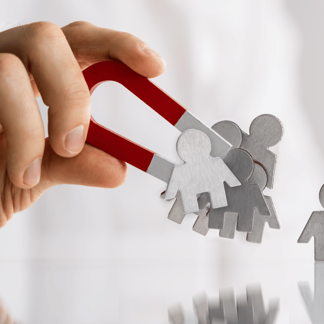 Hand holding a magnet attracting small paper cut-out people; recruitment concept.
