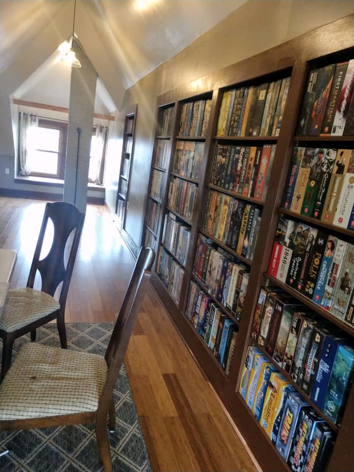 A dining room with a table and chairs and shelves filled with board games.