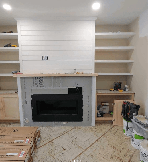 A living room with a fireplace and shelves being built