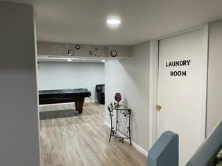 A laundry room in a basement with a pool table.