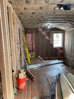 A room under construction with a bucket of home depot insulation and a ladder.