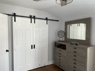 A bedroom with sliding barn doors , a dresser , and a mirror.