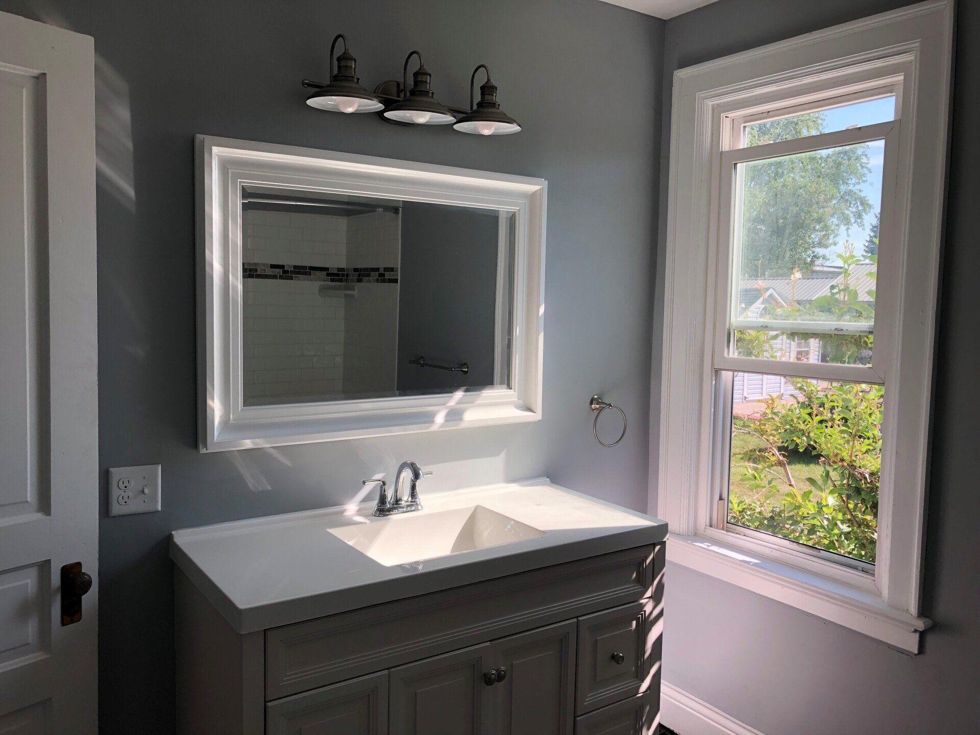 A bathroom with a sink , mirror and window.