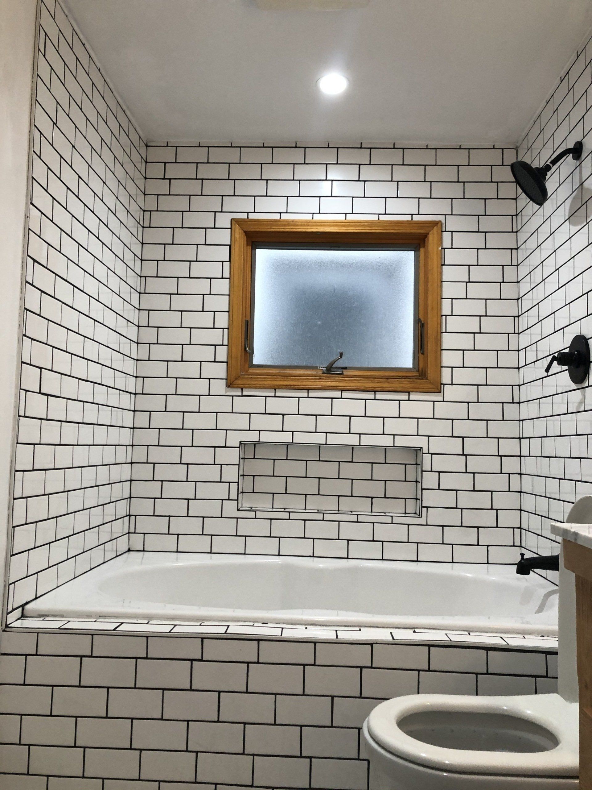 A bathroom with white brick walls , a tub , a toilet , and a window.