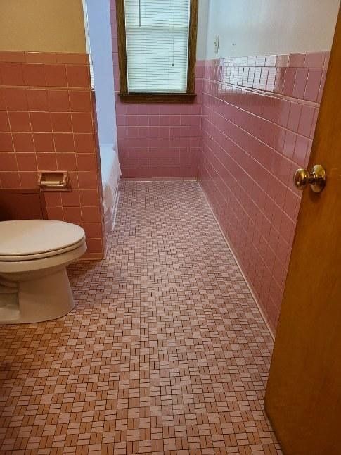 A bathroom with pink tiles and a toilet.