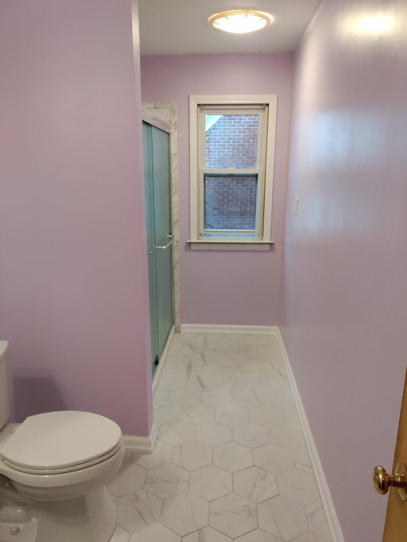 A bathroom with purple walls , a toilet , and a window.