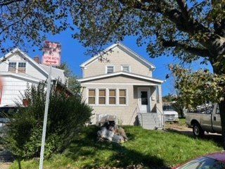 A dog is sitting in front of a house with a truck parked in front of it.