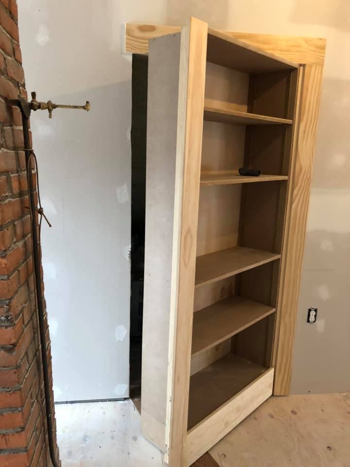 A wooden bookshelf is sitting in a room next to a brick wall.