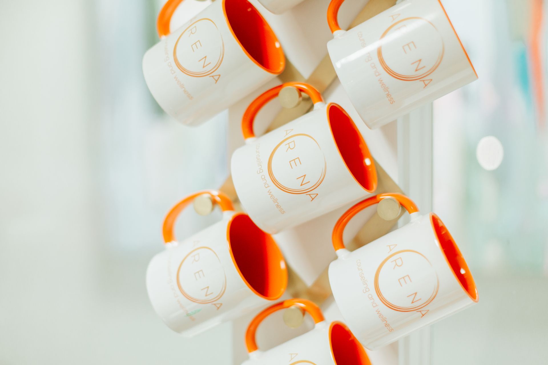 A bunch of coffee mugs with orange handles are hanging on a rack.