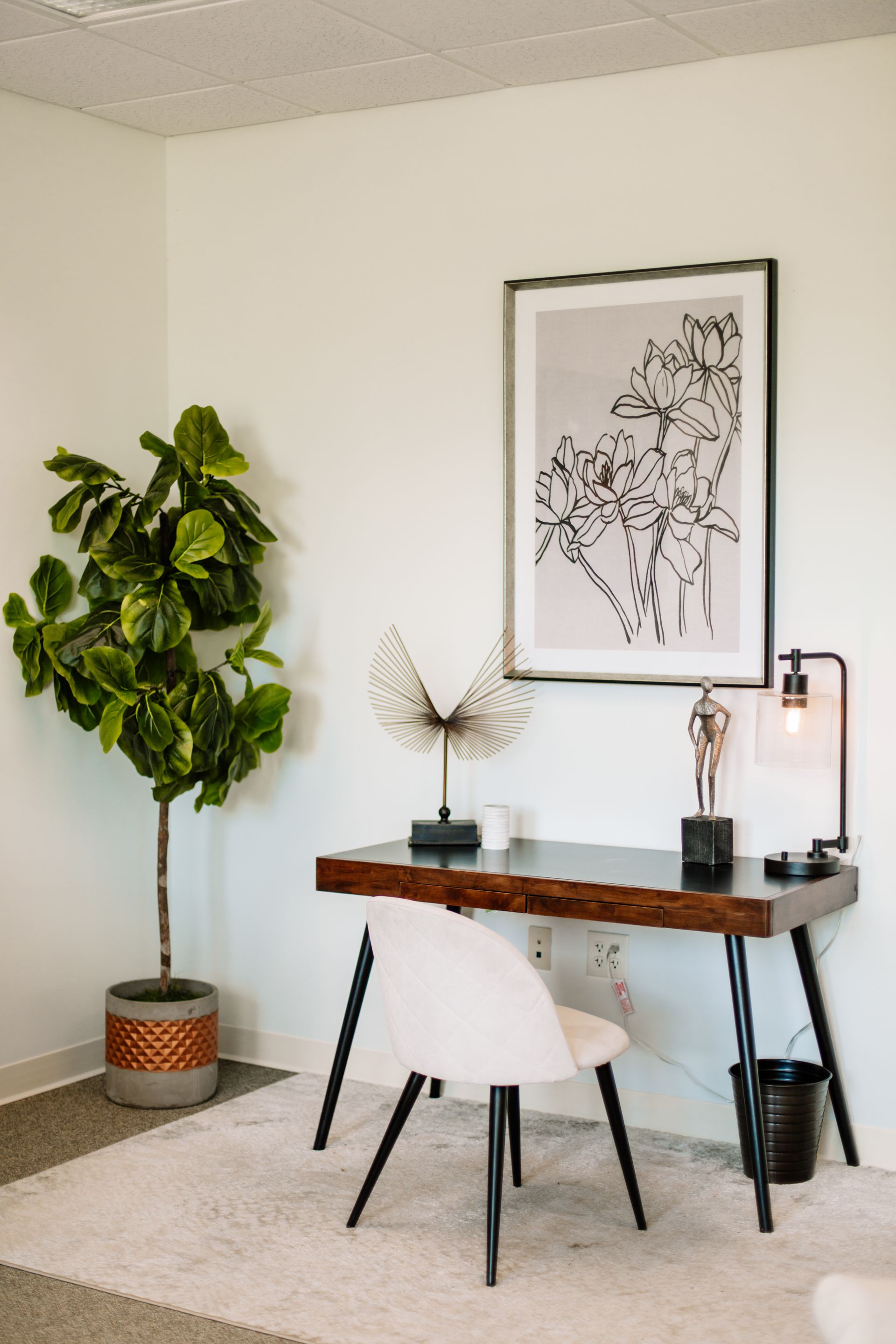 A room with a desk , chair , lamp and a picture on the wall.