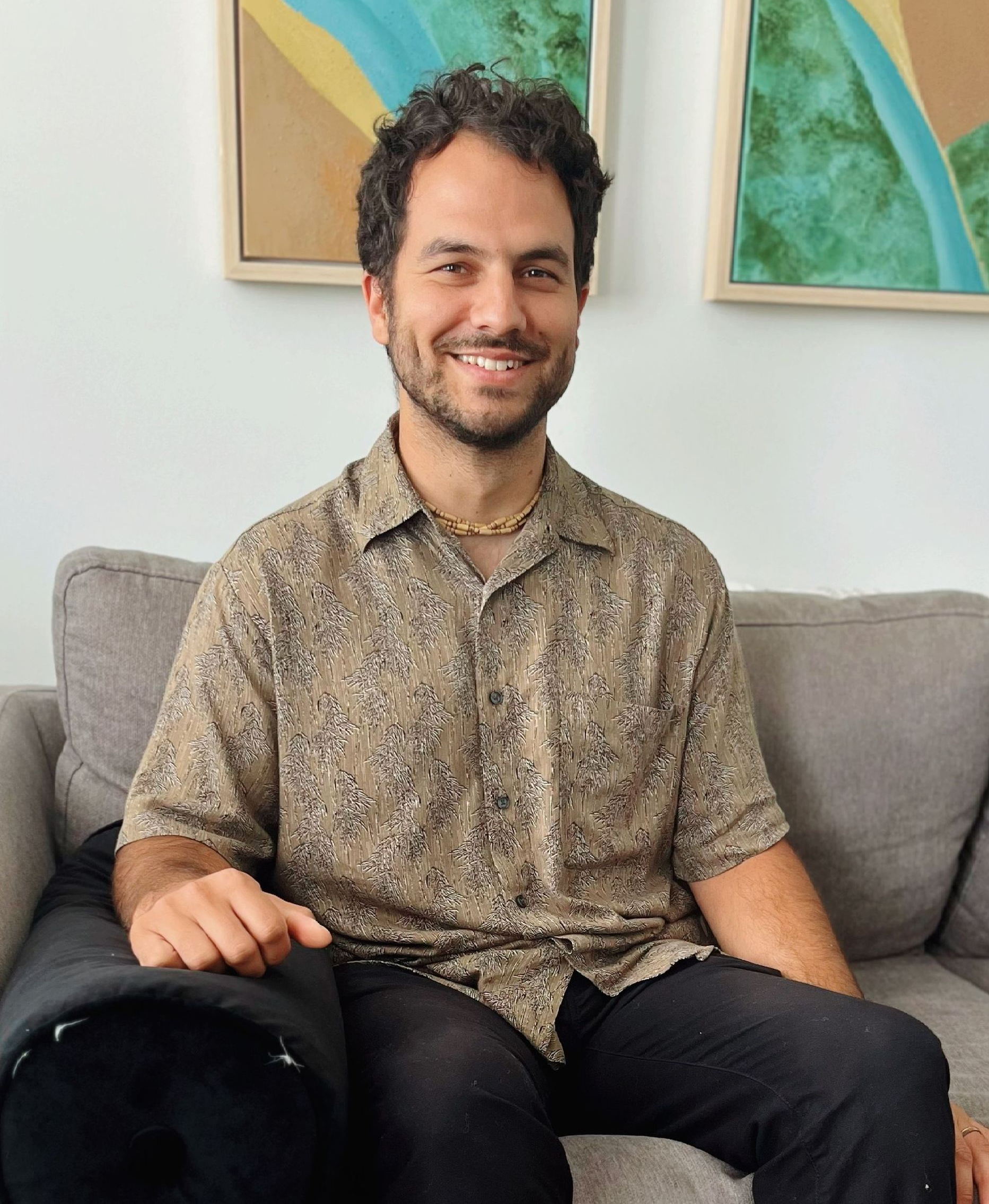 A man with a beard is comfortably sitting on a couch and smiling.
