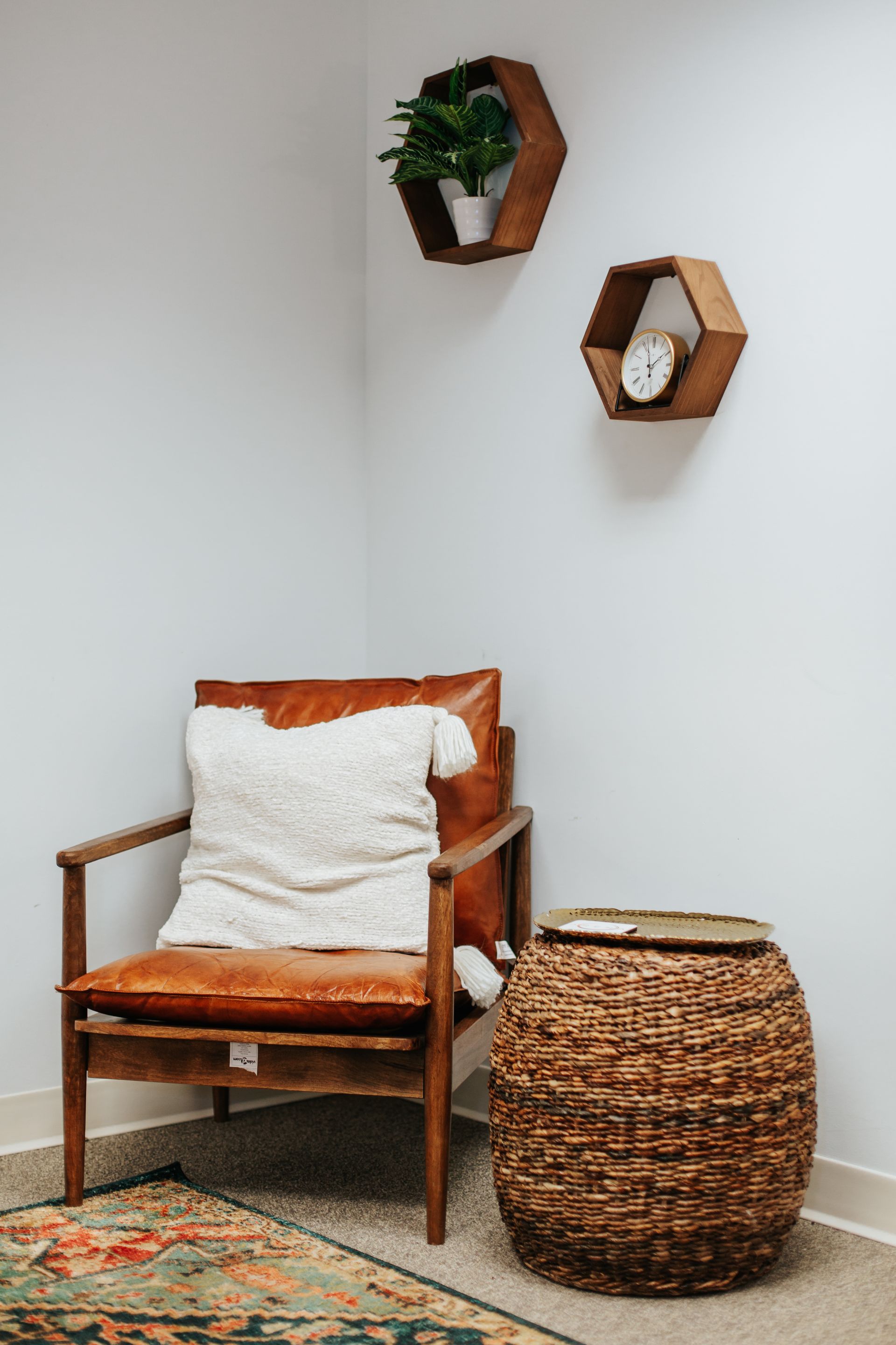 A chair with a pillow on it is sitting in a corner of a room next to a wicker stool.