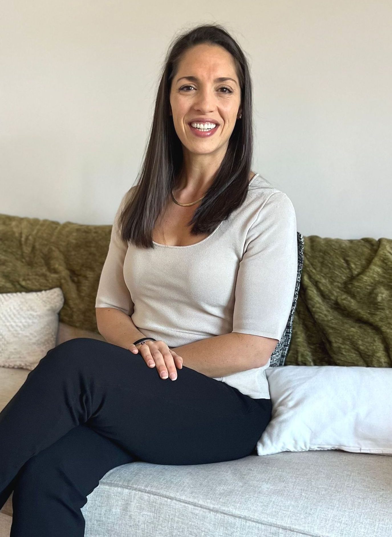 A woman is sitting on a couch with her legs crossed and smiling.