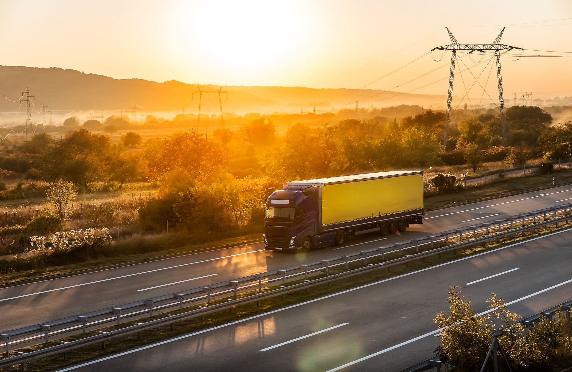 Semi-truck on highway at sunrise, yellow cargo trailer, sunlit landscape.
