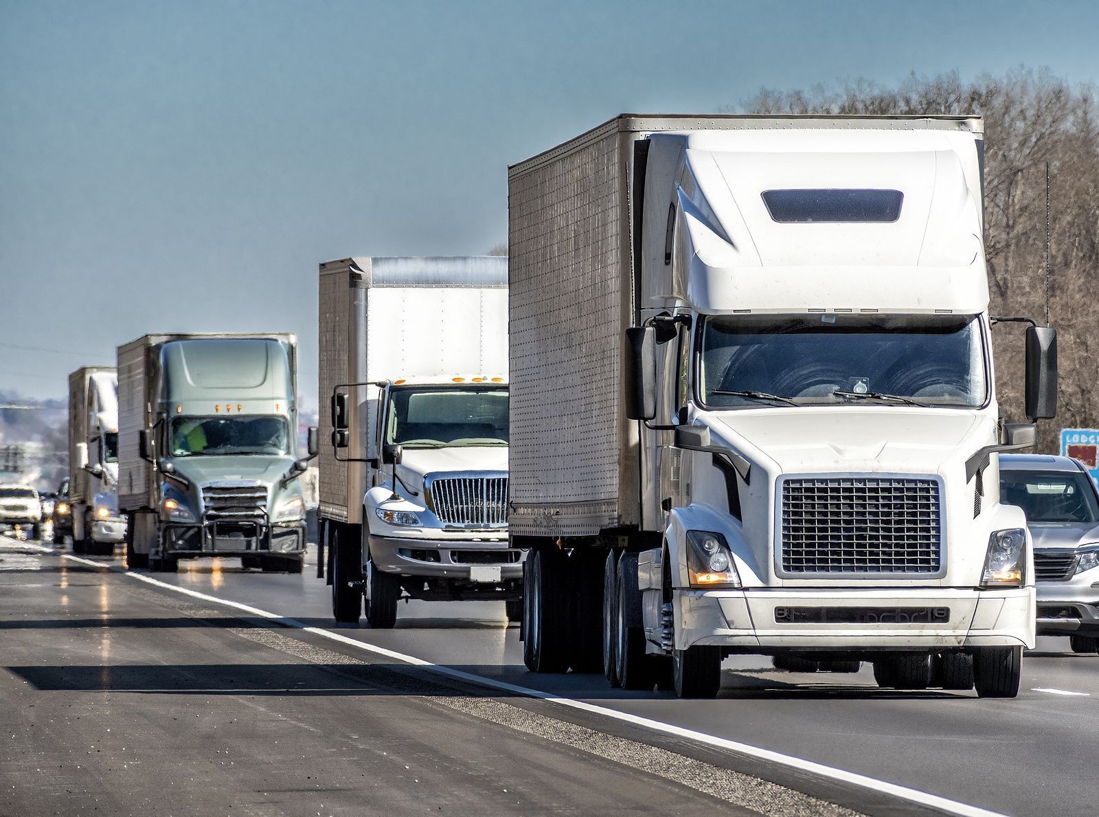 A row of semi trucks are driving down a highway.