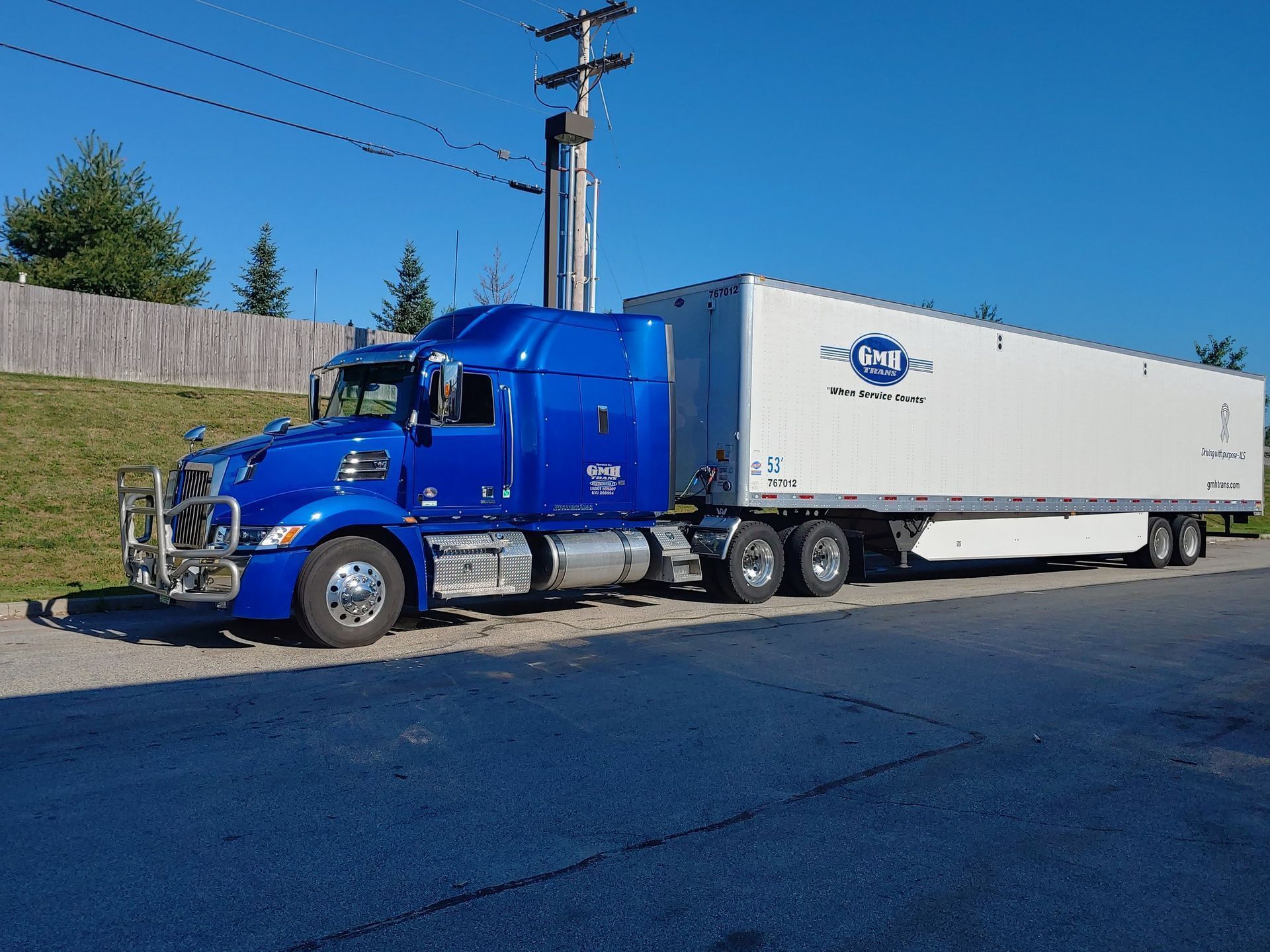 A blue semi truck with a white trailer is parked on the side of the road.