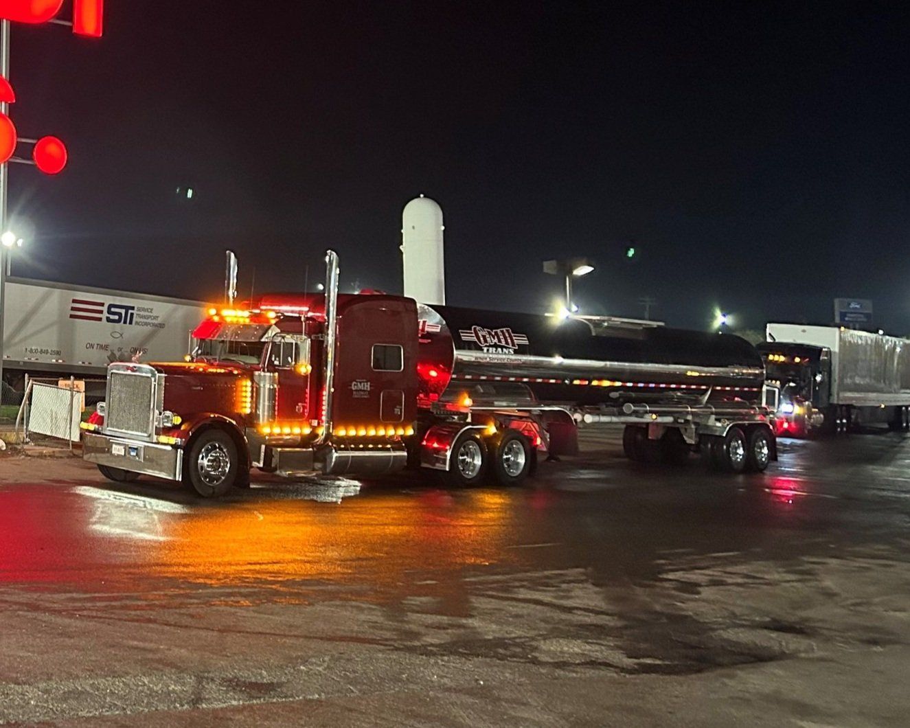 A red semi truck is parked in a parking lot at night.