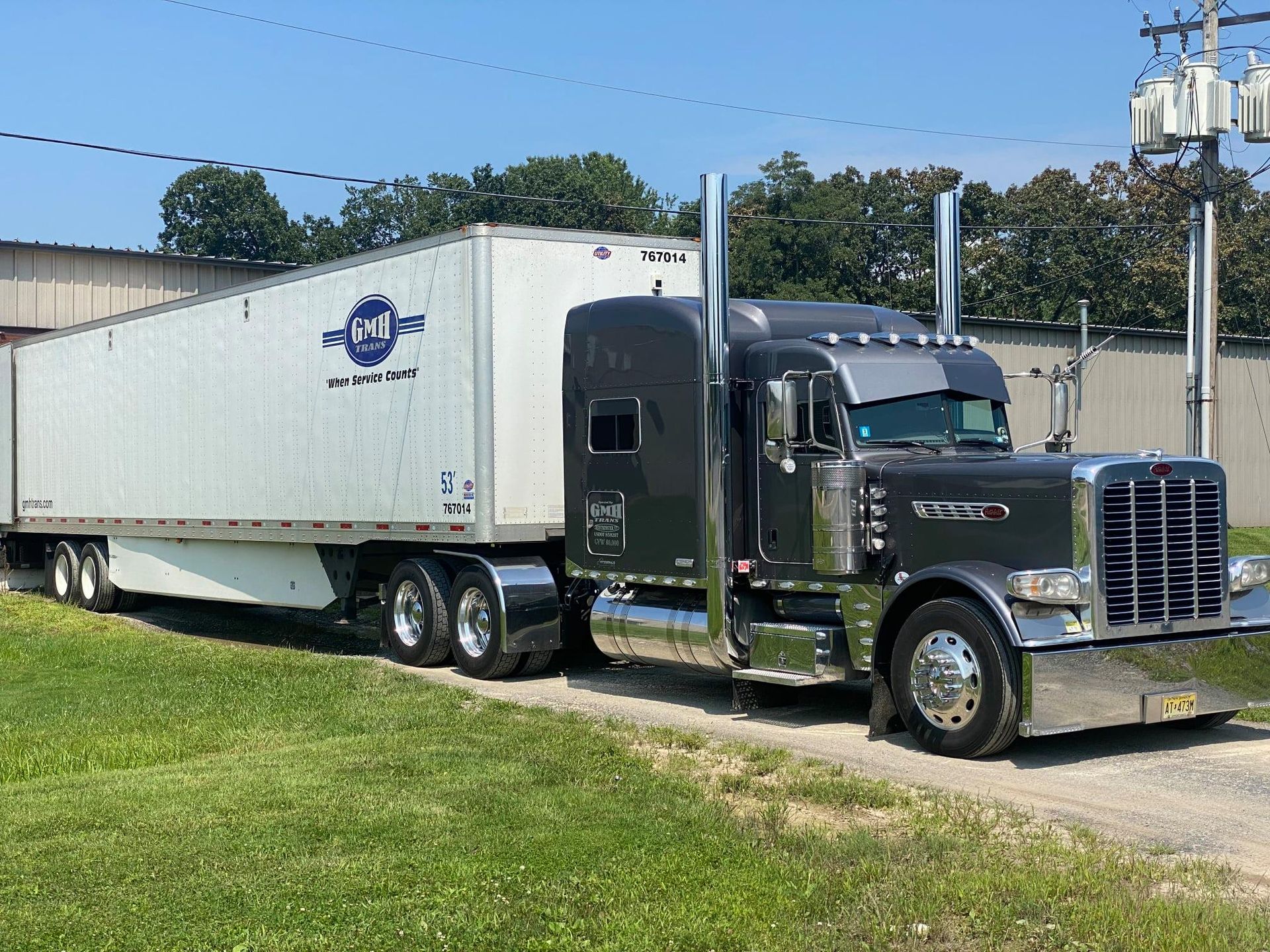 Dark gray semi-truck with chrome accents and white trailer parked on a gravel area.