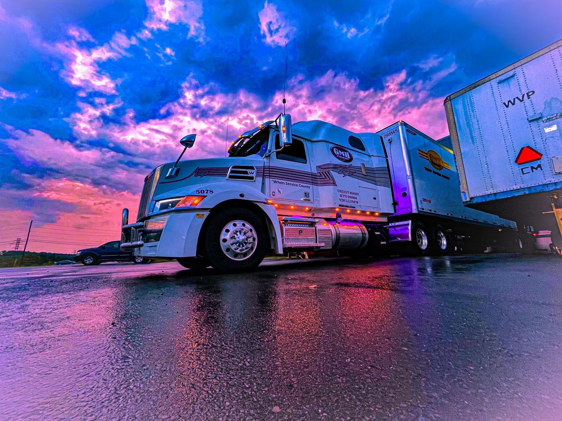 A semi truck is parked on the side of the road at sunset.