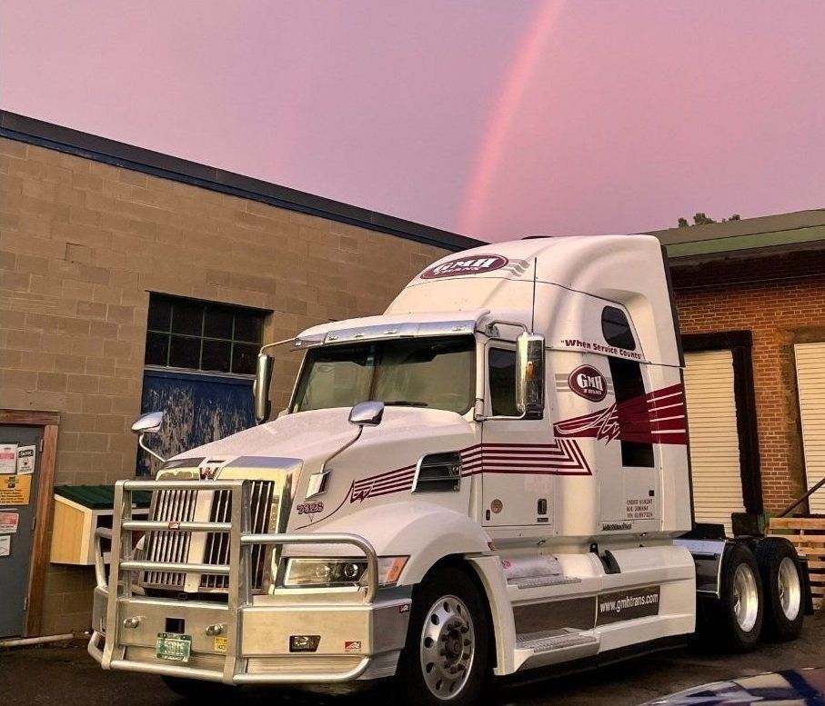 A semi truck is parked in front of a building with a rainbow in the sky