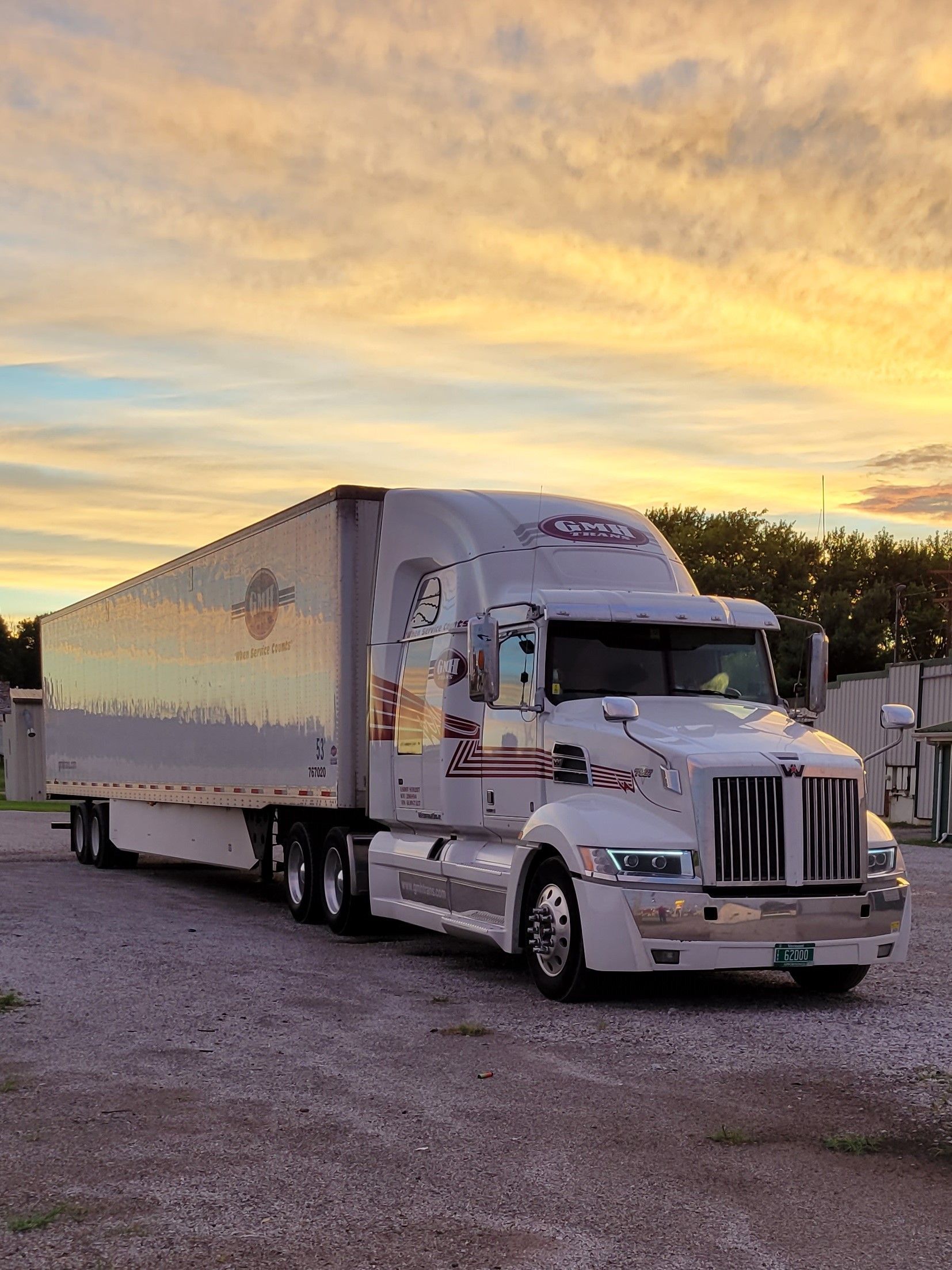 A semi truck is parked in a gravel lot at sunset.