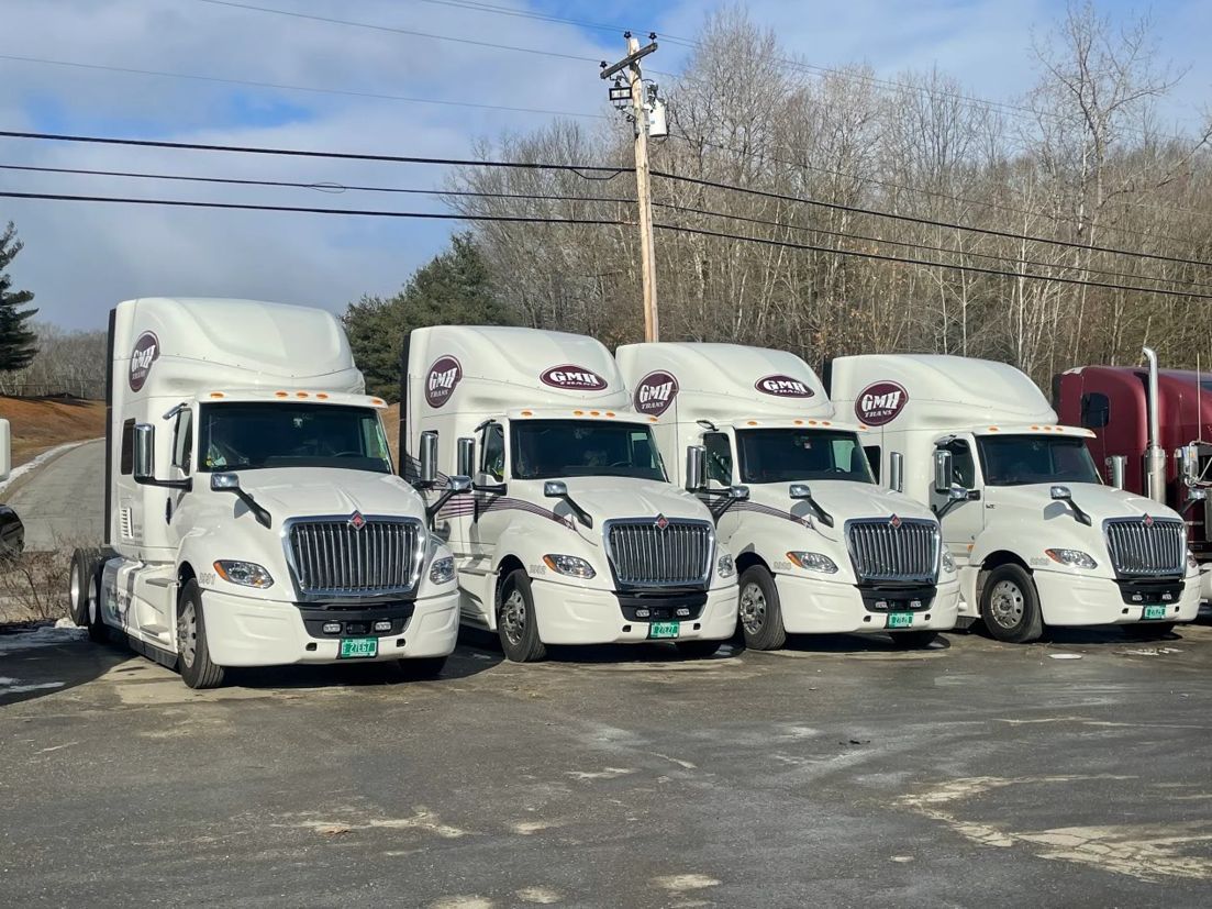 A row of white semi trucks are parked in a parking lot.