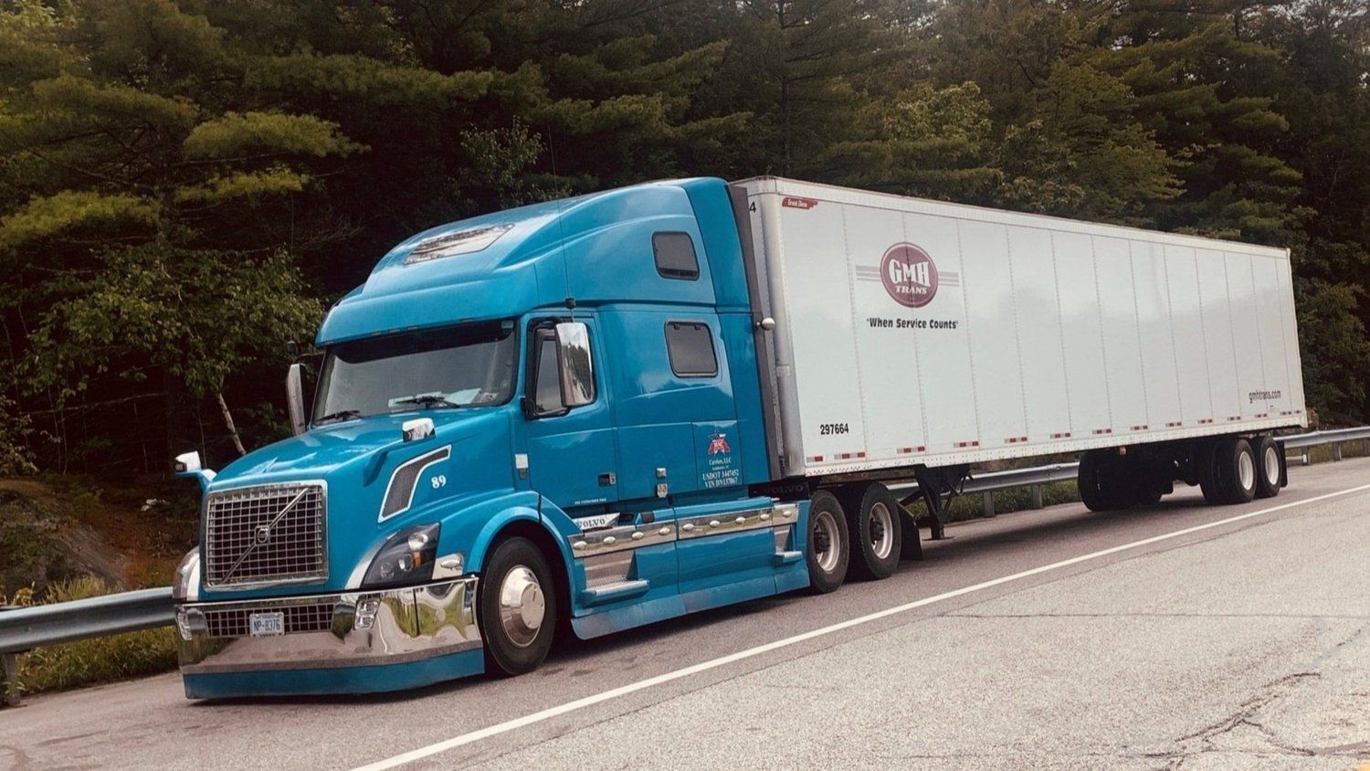 A blue semi truck with a white trailer is parked on the side of the road.