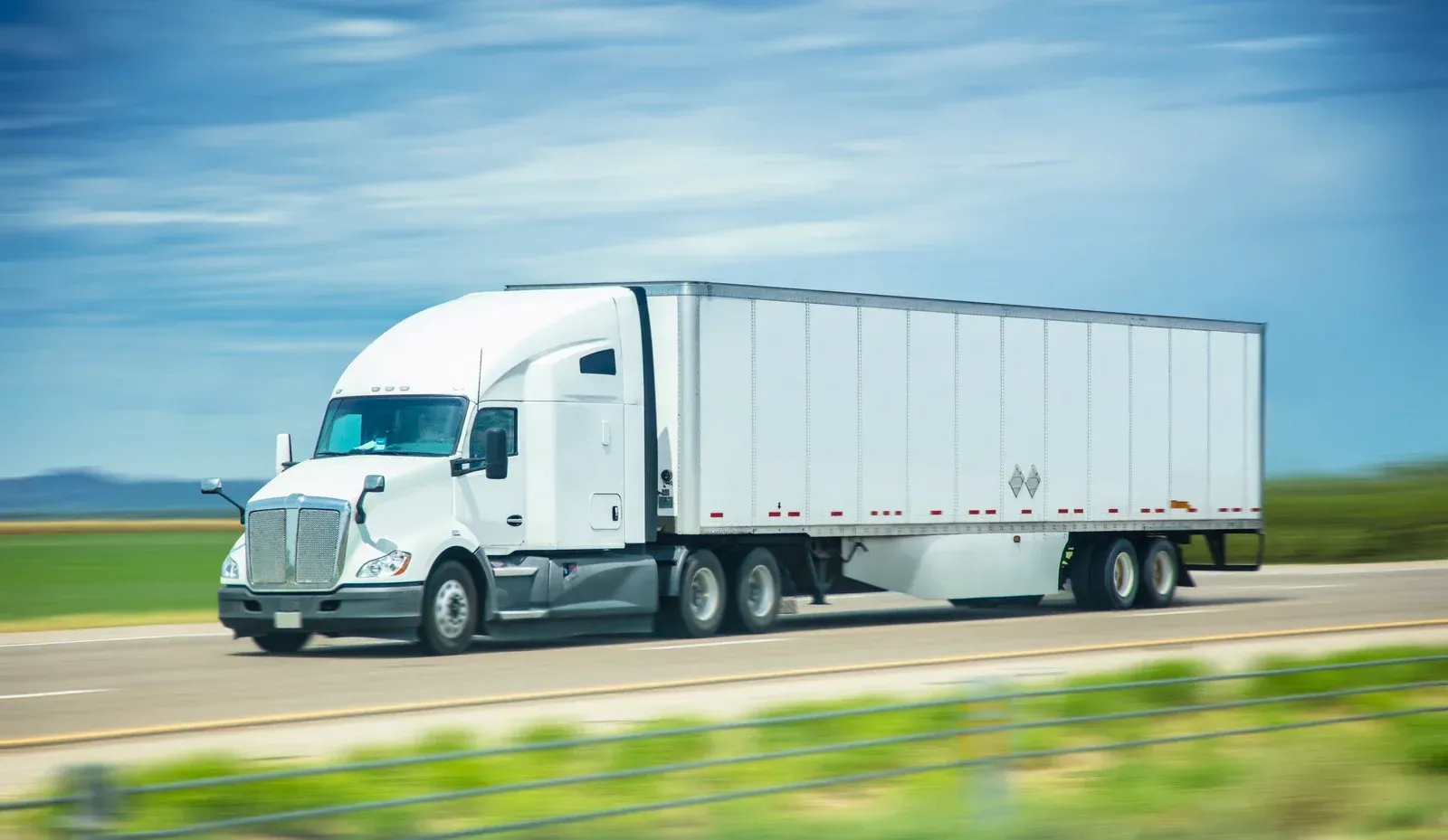 A white semi truck is driving down a highway.