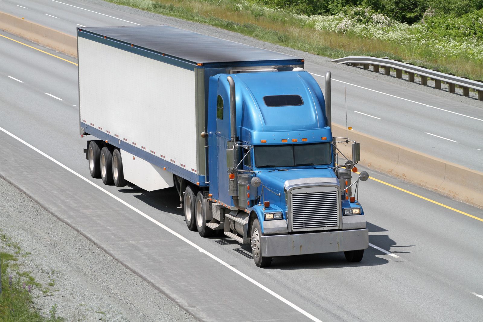 A blue semi truck with a white trailer is driving down a highway.