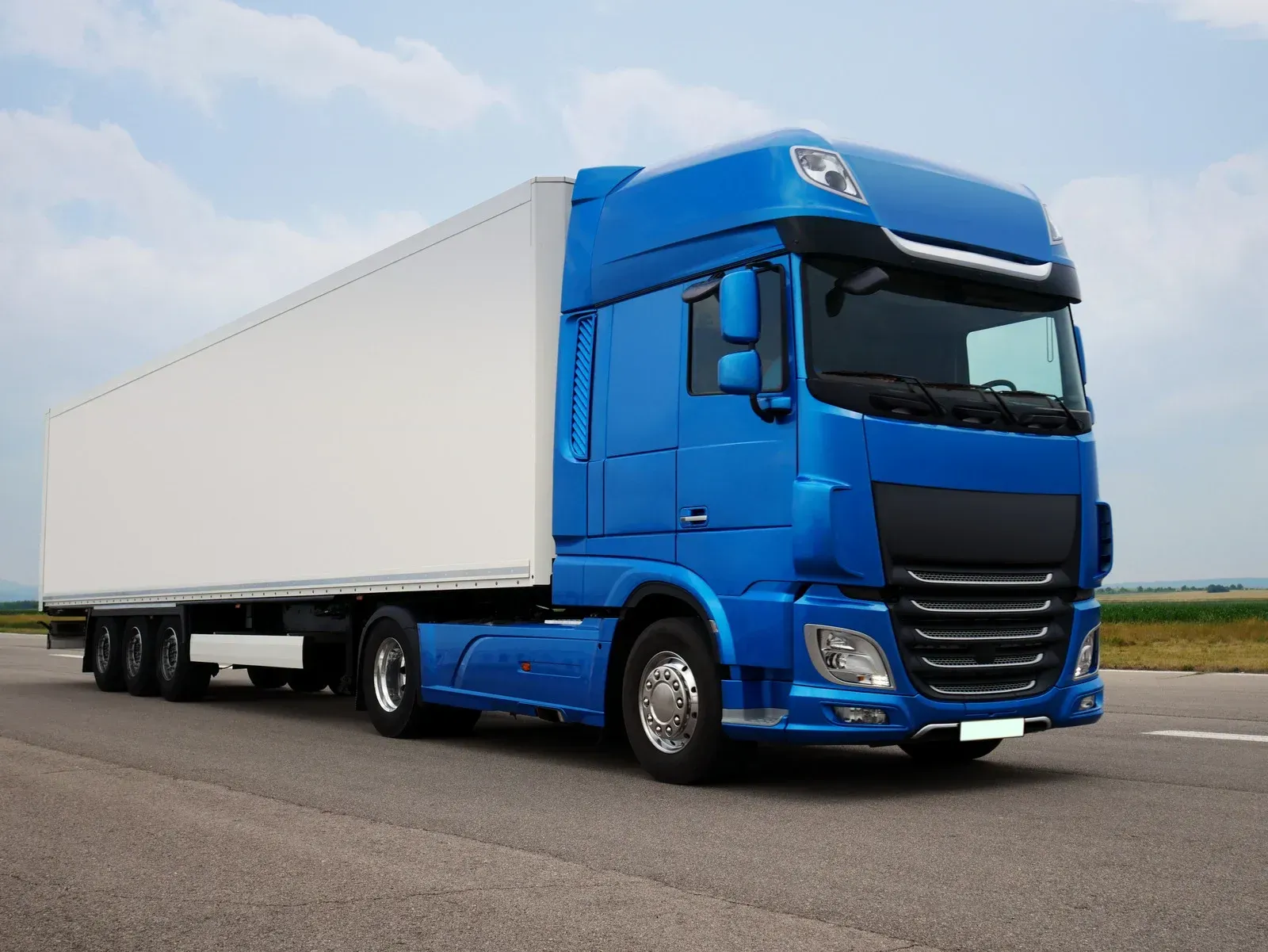A blue semi truck with a white trailer is driving down a road.