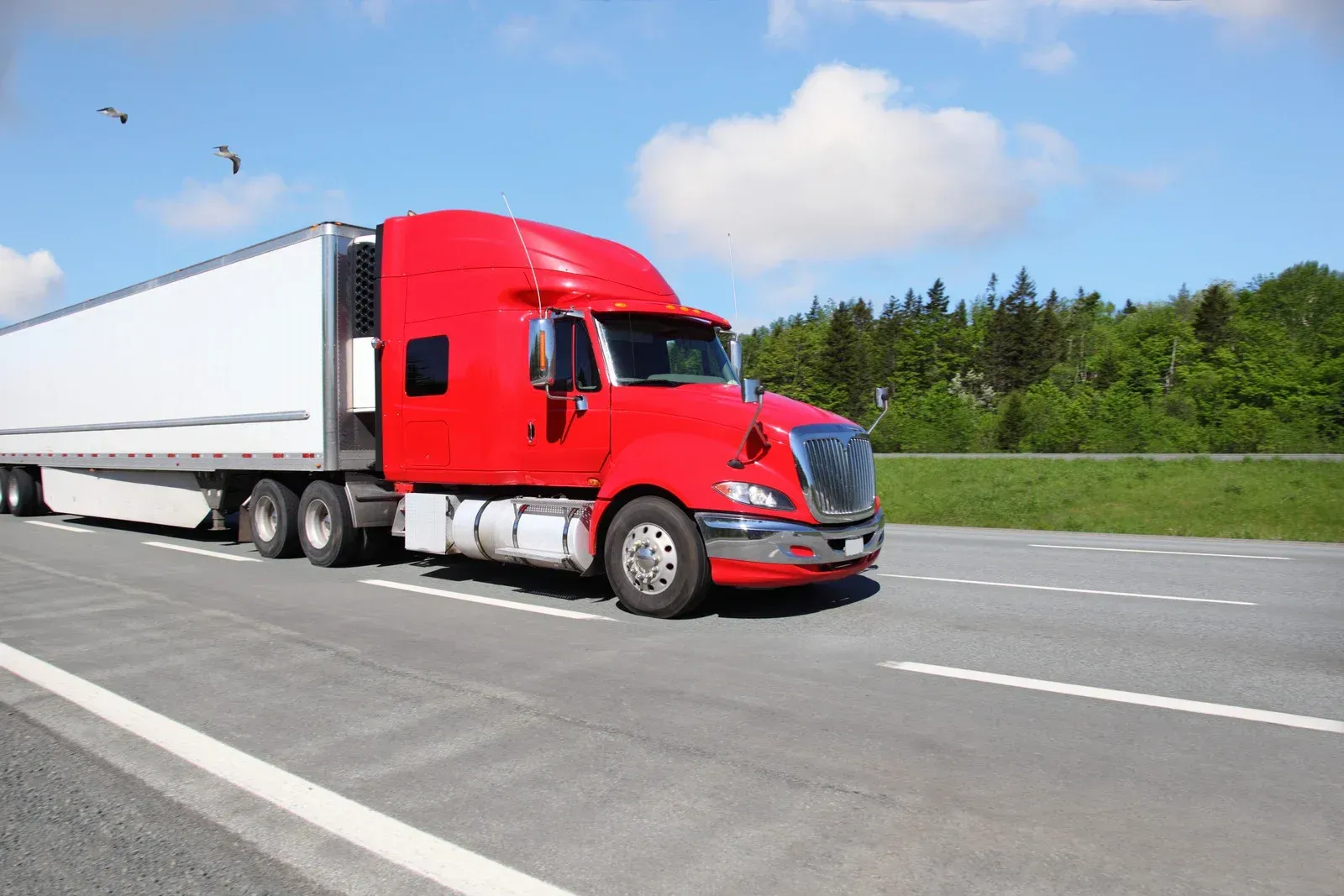 A red semi truck with a white trailer is driving down a highway.