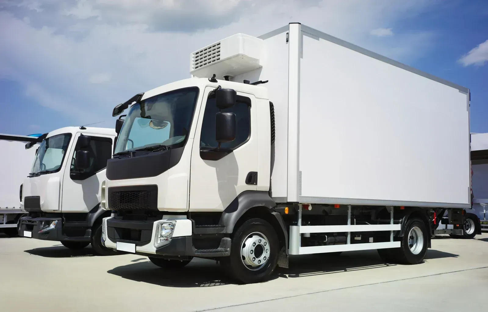 Two white refrigerated trucks are parked next to each other in a parking lot.