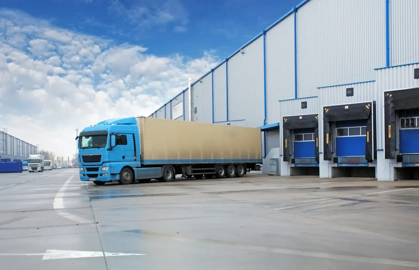 A blue semi truck is parked in front of a warehouse.