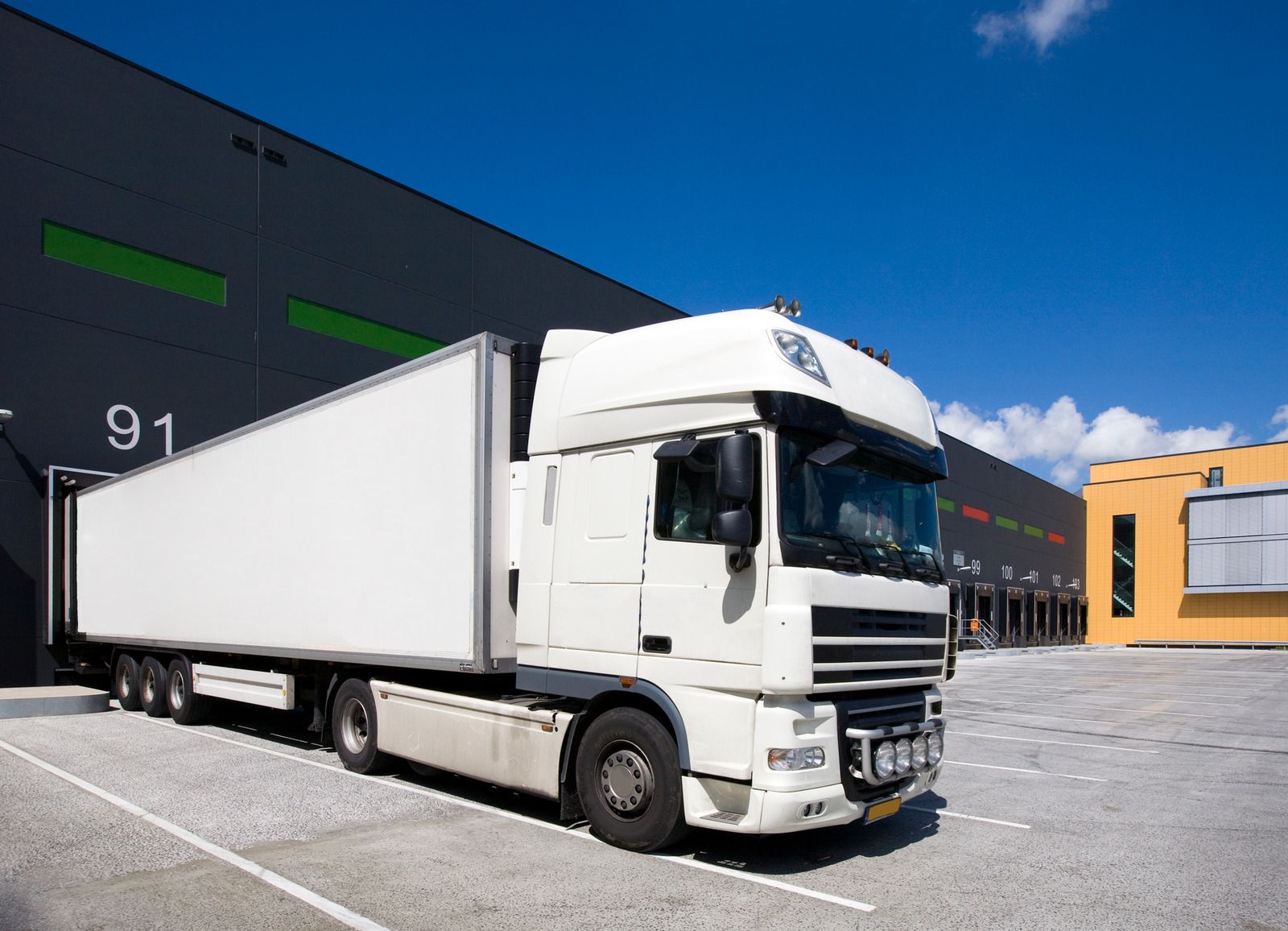A white semi truck is parked in front of a warehouse.