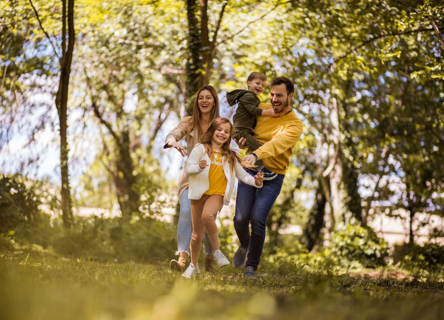 Family of four running through a park, smiling.