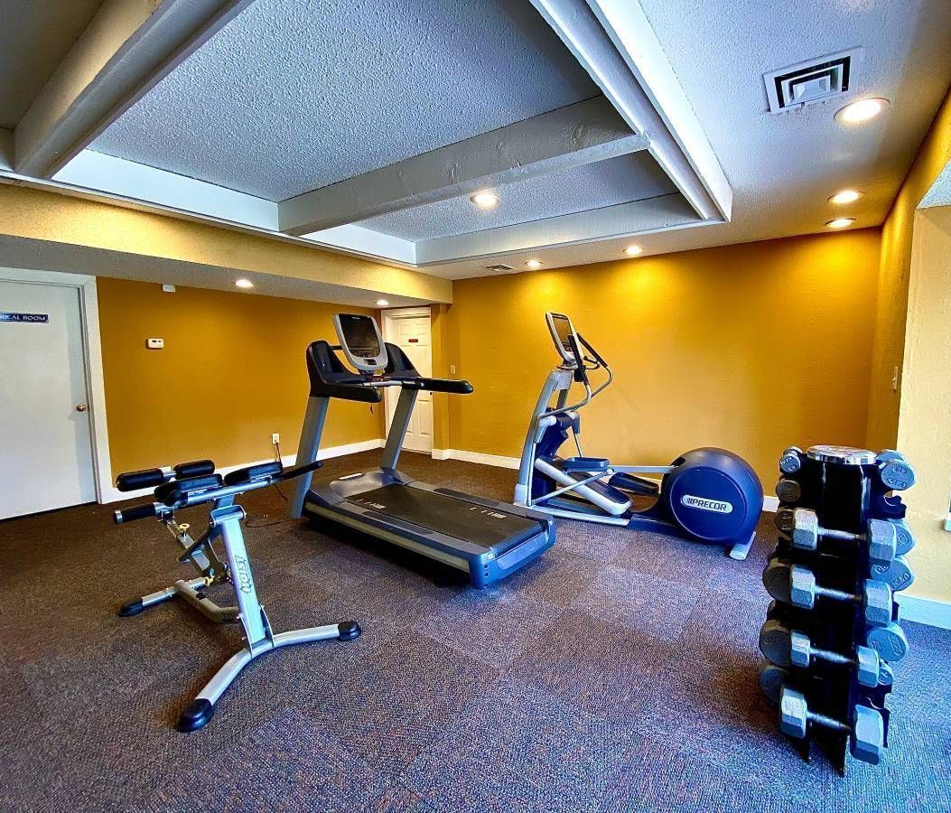 Small gym with a treadmill, elliptical, free weights, and yellow walls.