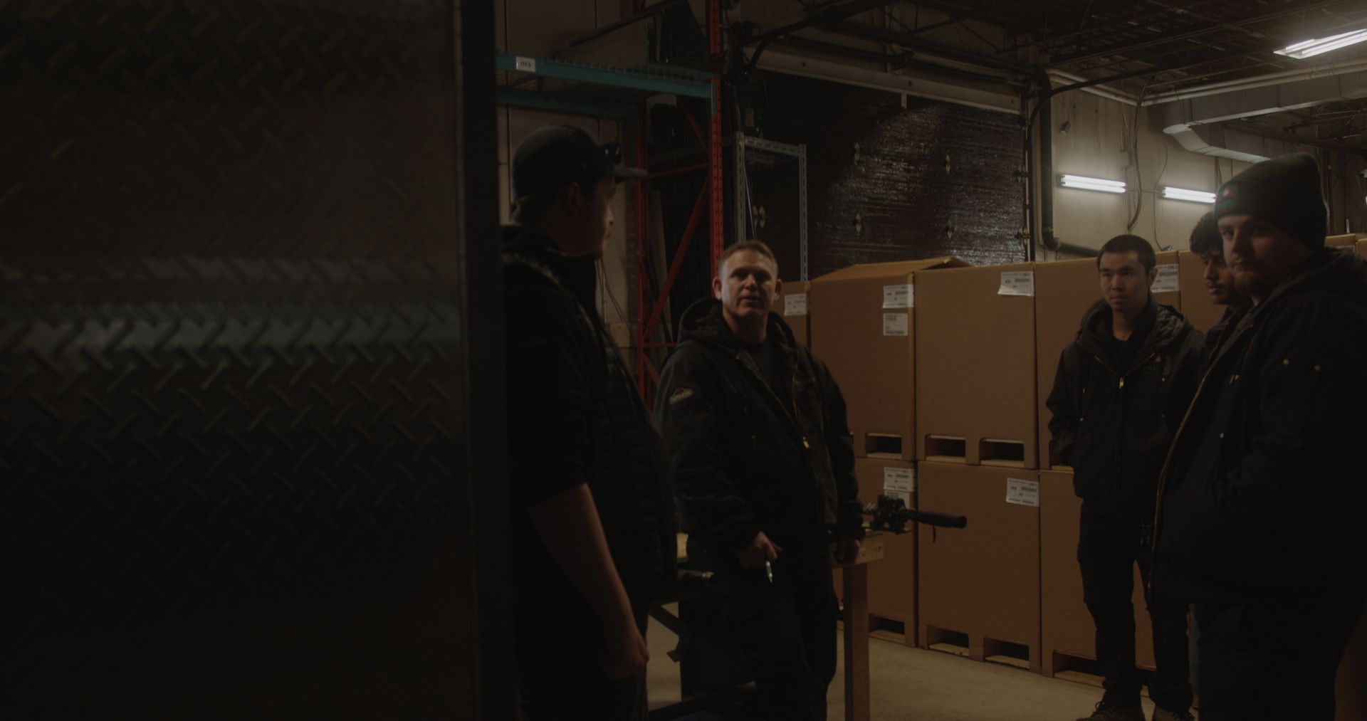 A group of men are standing in a dark room with boxes.