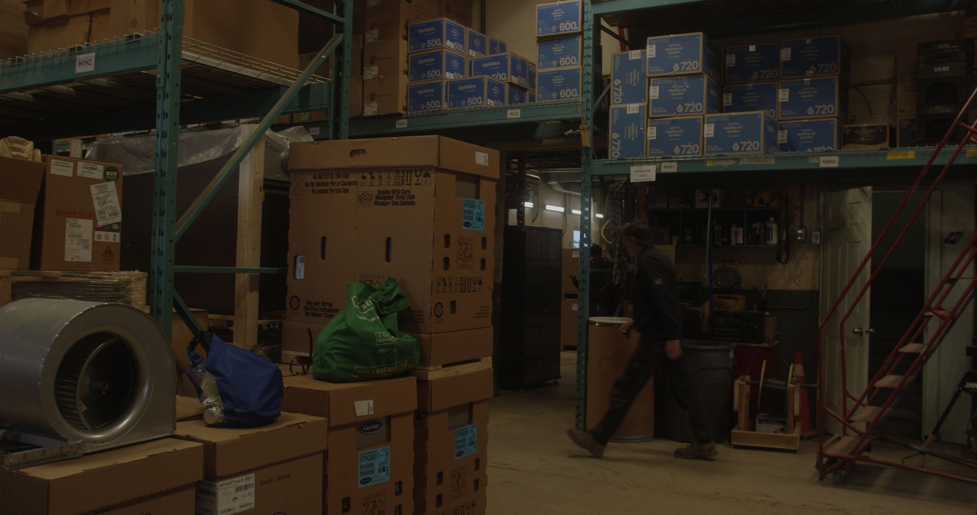 A man is walking through a warehouse filled with lots of boxes.