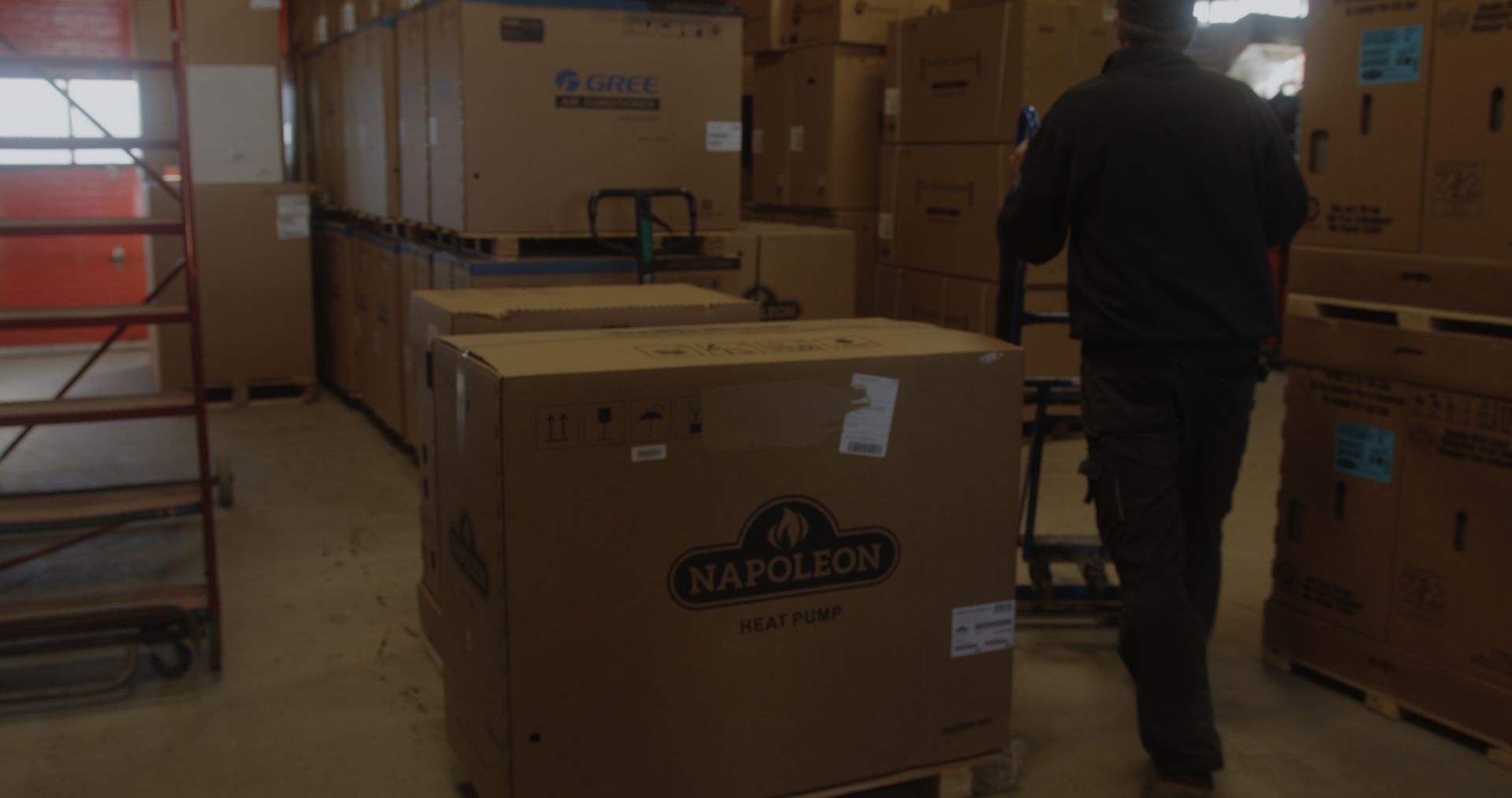 A man is pushing a cardboard box on a pallet in a warehouse.