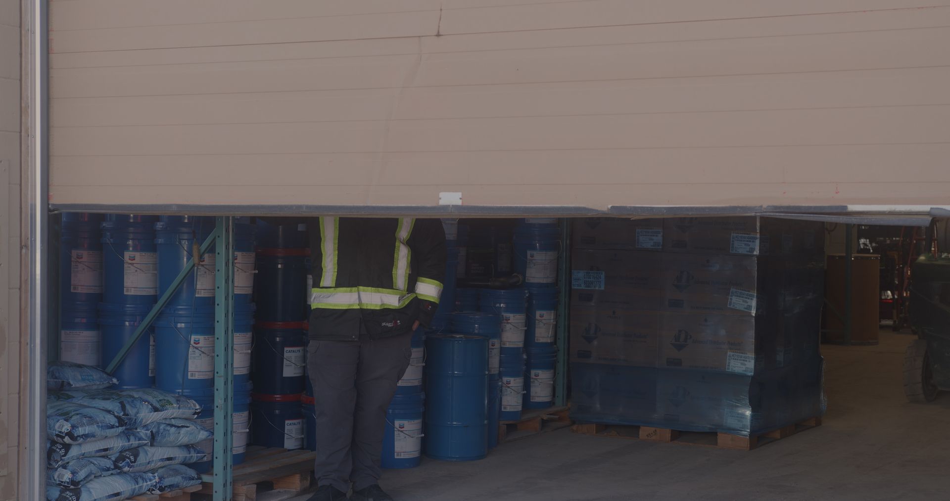 A man is standing in a warehouse filled with barrels and pallets.