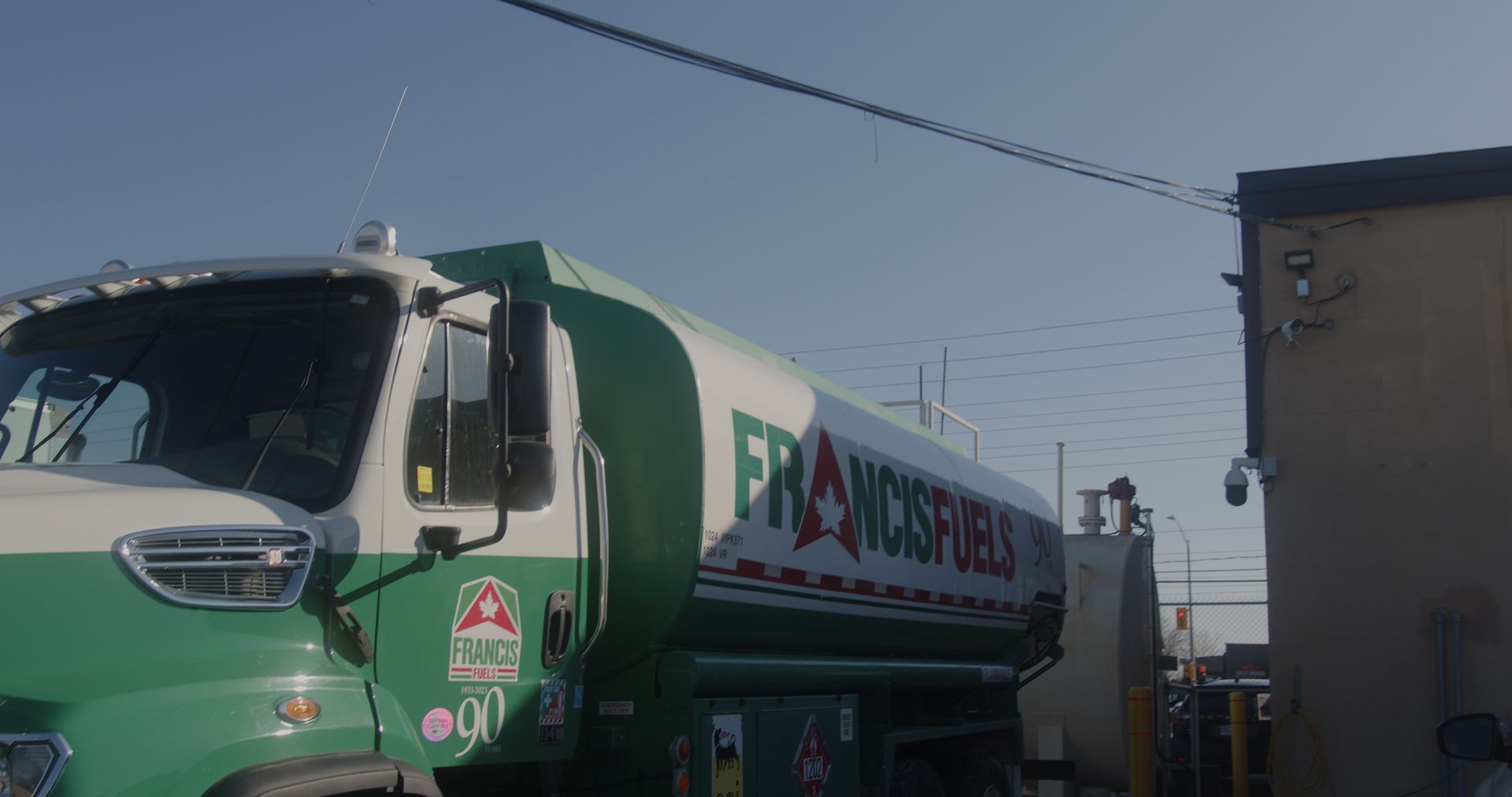 A green and white tanker truck is parked in front of a building.