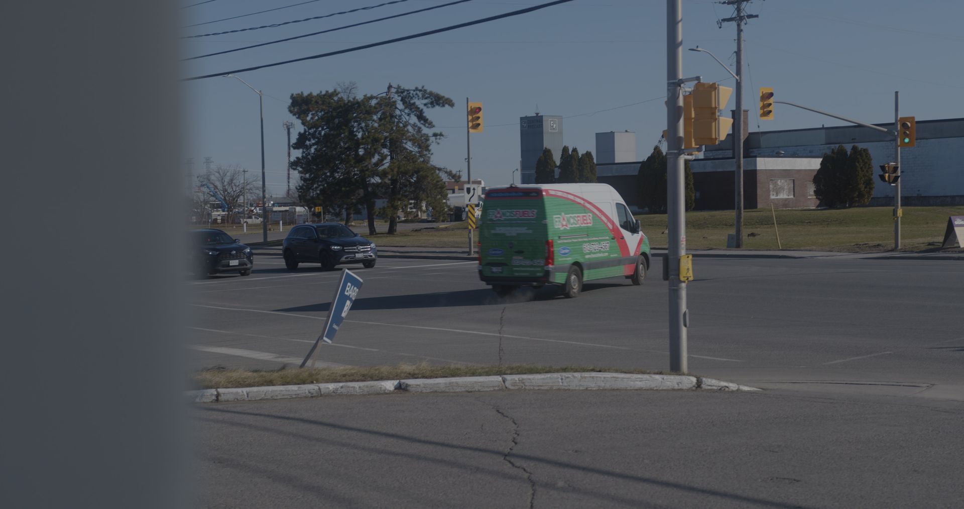 A green van is driving down a street at an intersection.