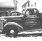 A black and white photo of an old truck parked in front of a building.