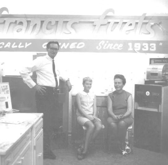 A black and white photo of three people in front of a sign that says