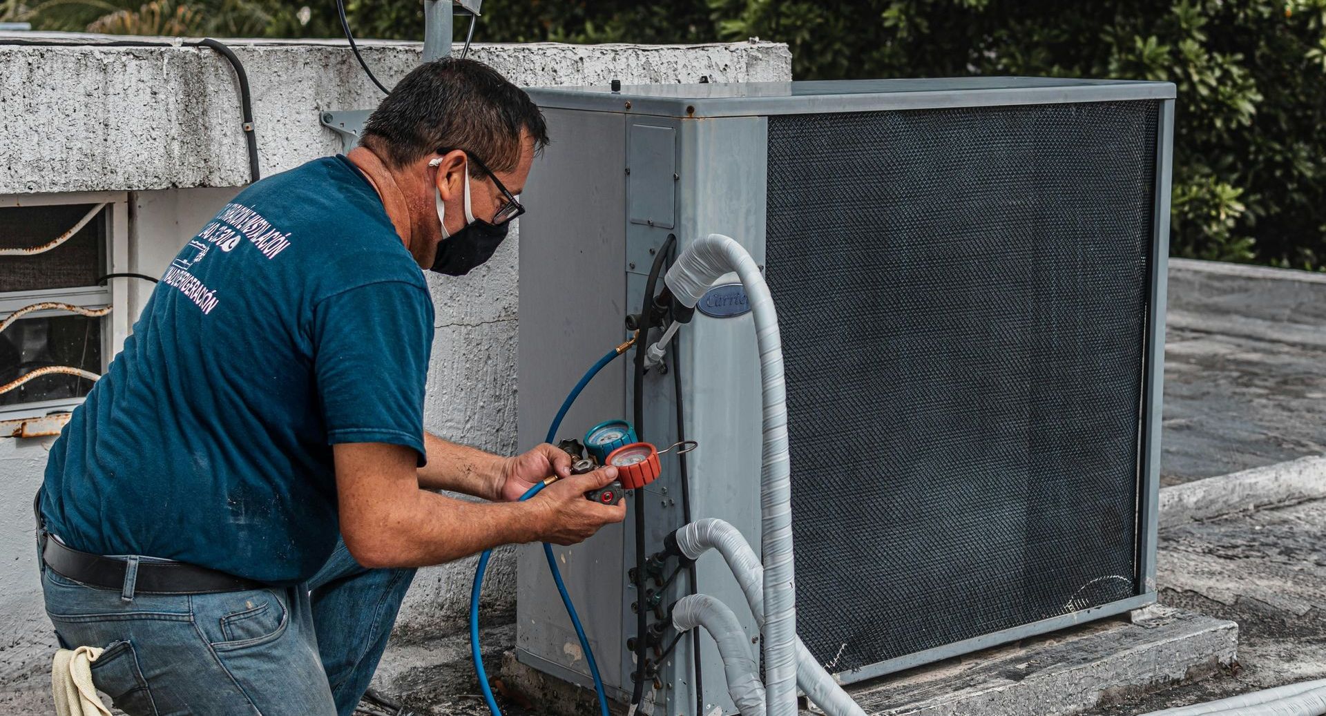 A man wearing a mask is working on an air conditioner on a roof.