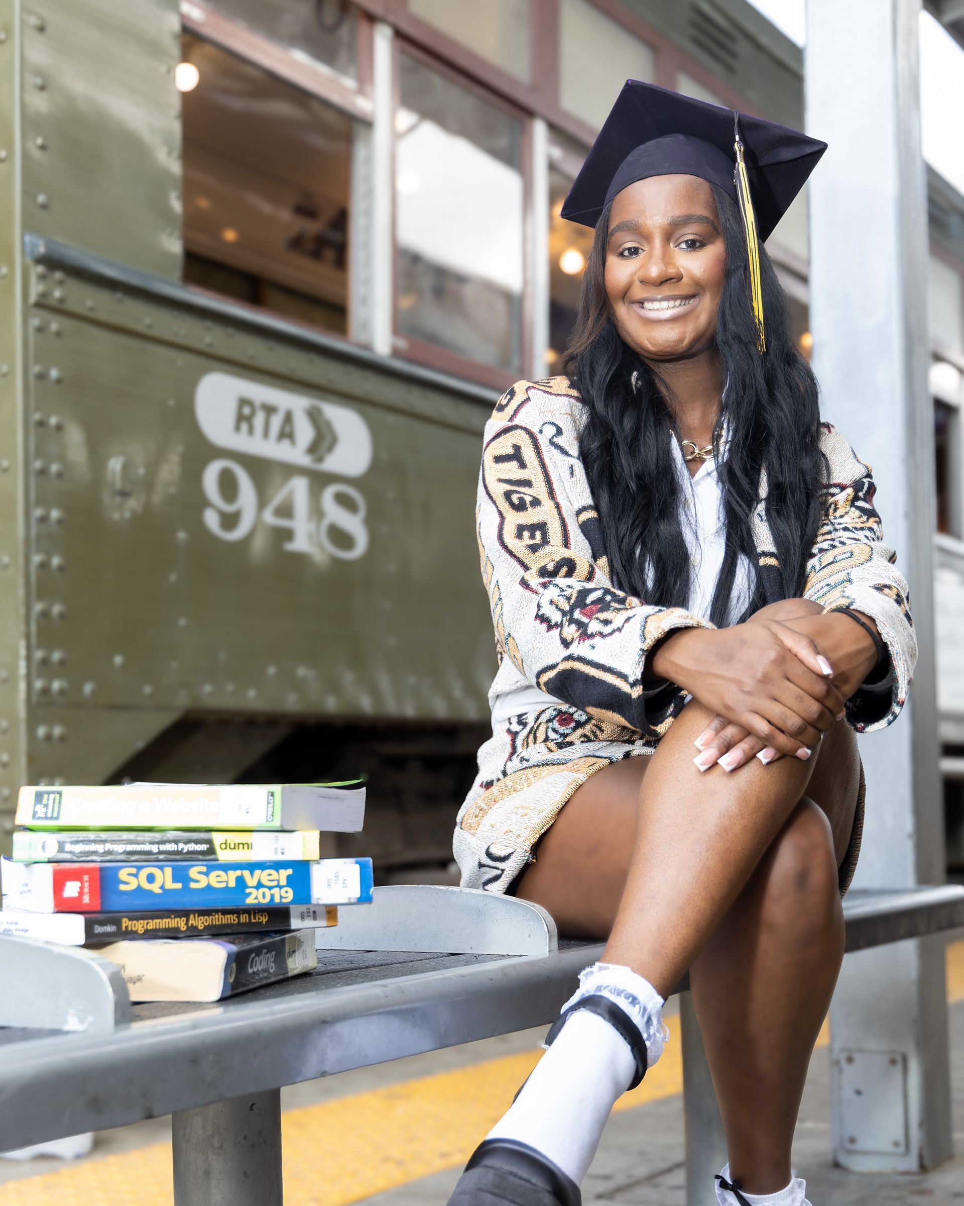 A woman in a graduation cap and gown is sitting on a bench