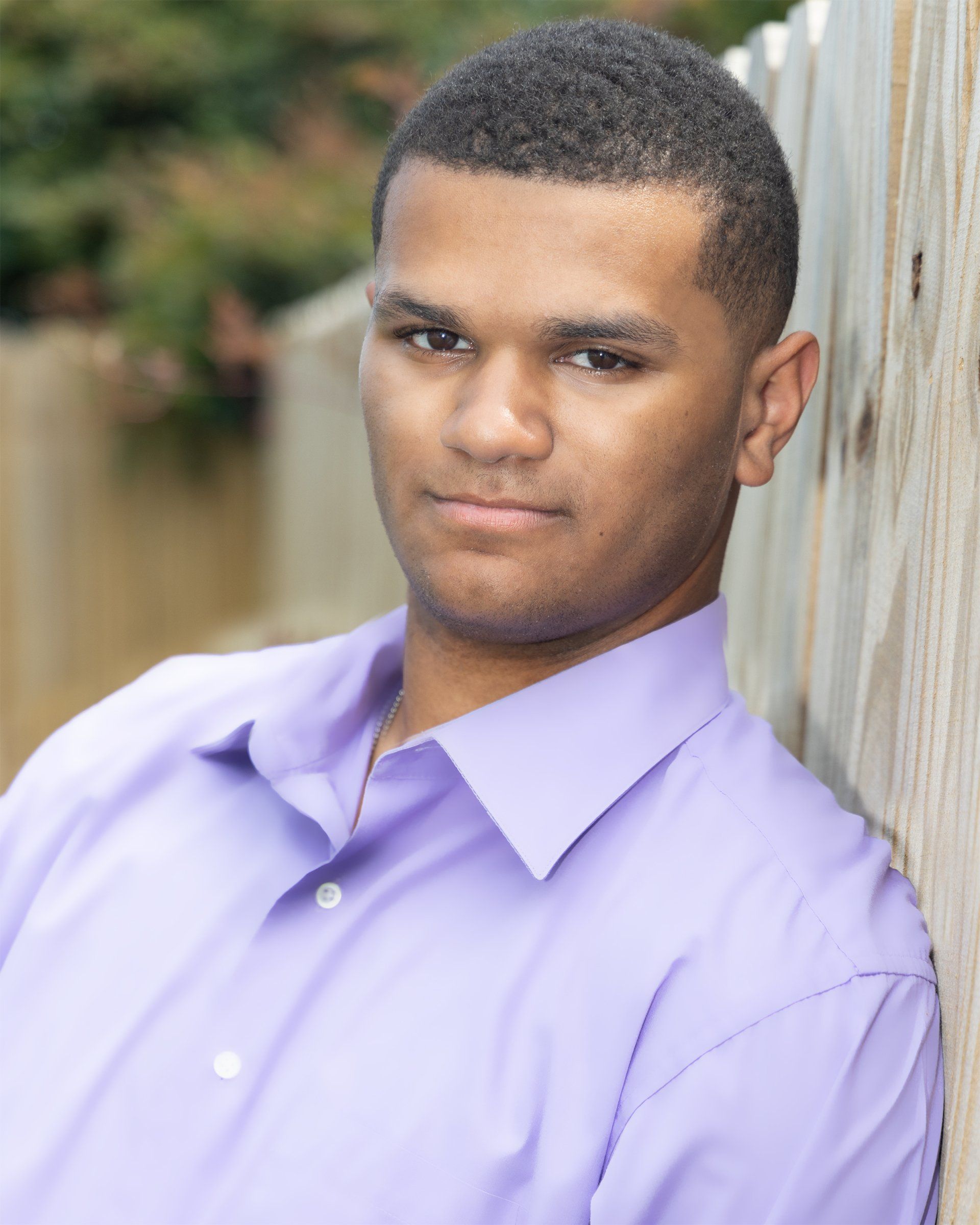 A man in a purple shirt leans against a wooden fence