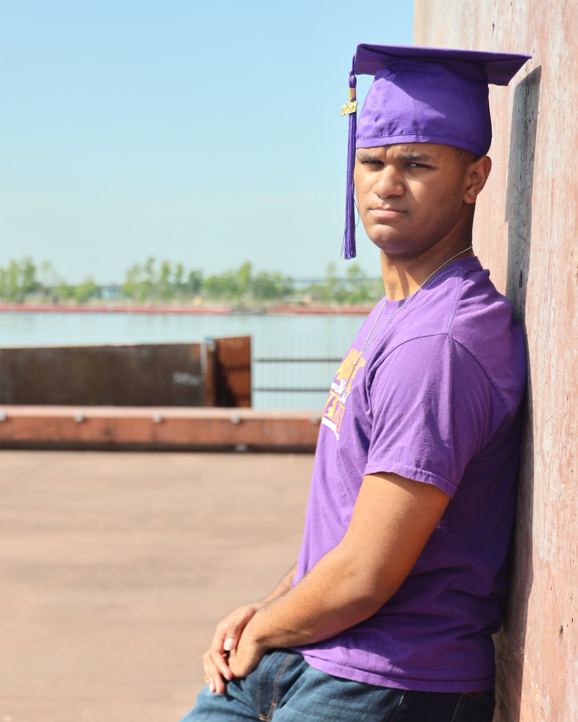 A man wearing a purple cap and gown leans against a wall